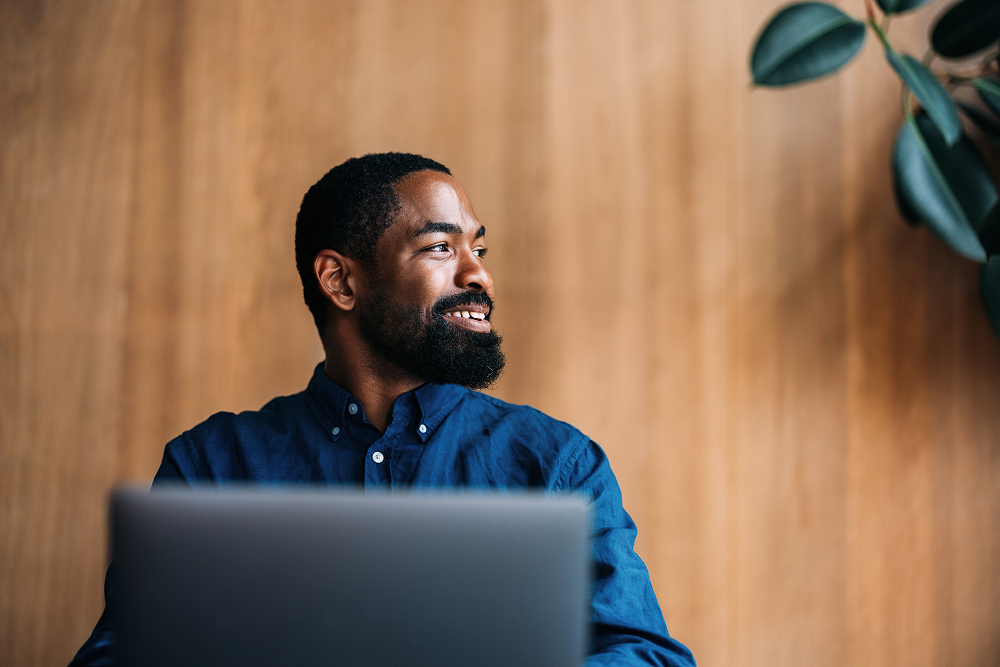 Portrayal of a Capella University online computer science student on his laptop in a conference room with wooden paneling.&nbsp;