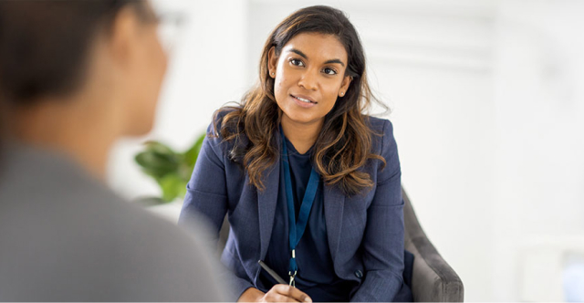 woman in blue blazer talking to someone while taking notes