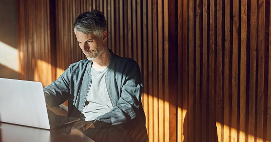 man using a laptop at a desk in front of a wooden wall