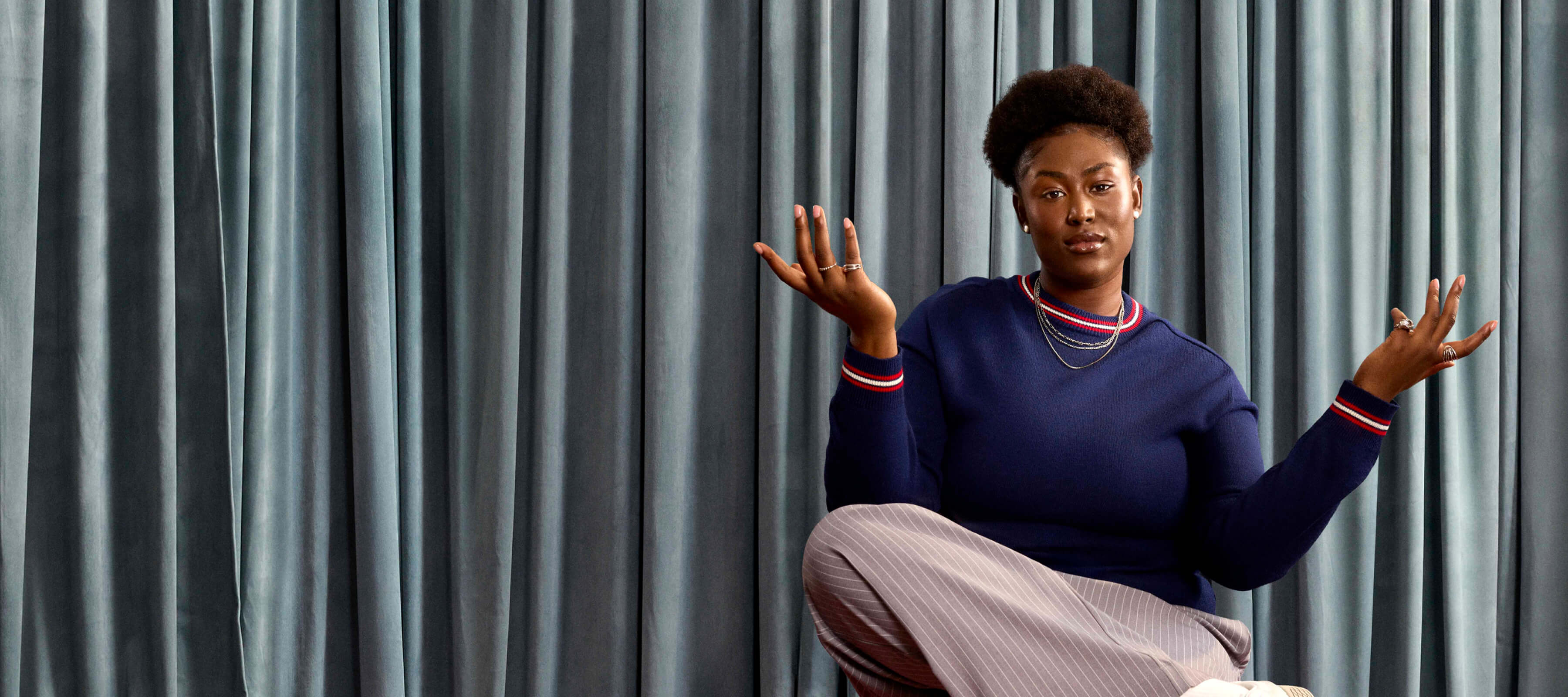 woman with hands up in the air with blue drapes behind her