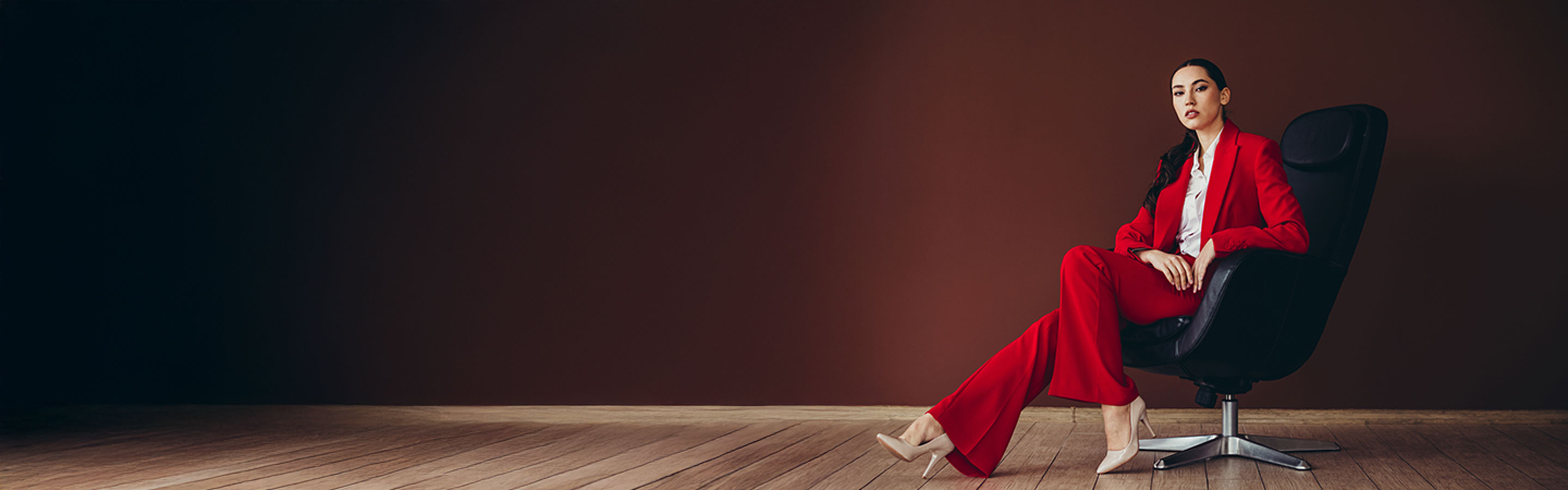 asian woman in bright red suite sitting in a leather chair