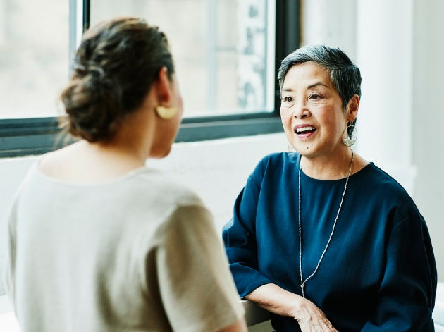 Two women having a friendly conversation near a window.